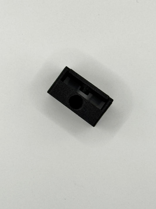 A small black textured plastic component with a circular hole, photographed on a plain light gray background.