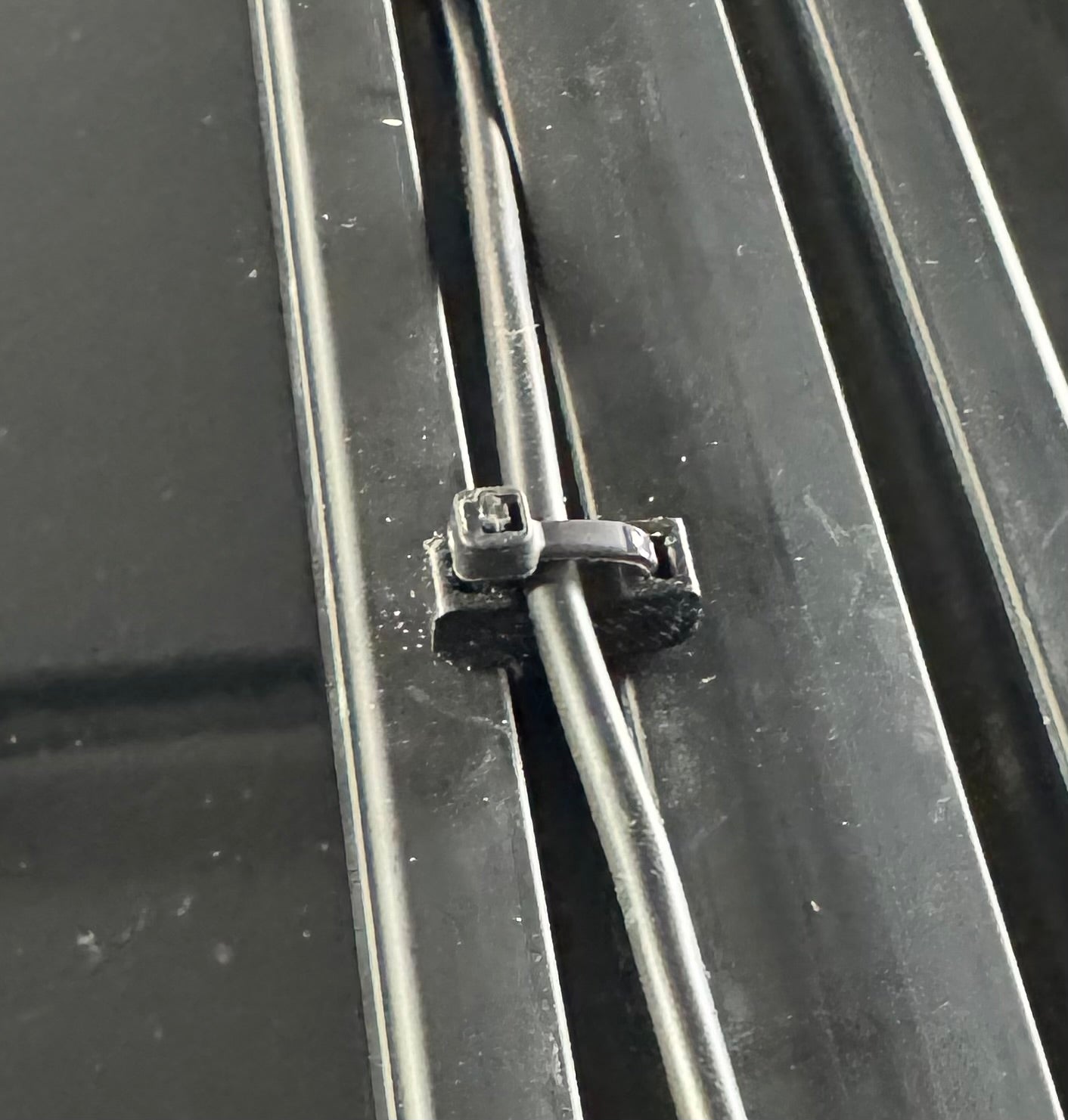 A 3D printed ziptie mount attached to a metal roof rack, used for organizing wiring.