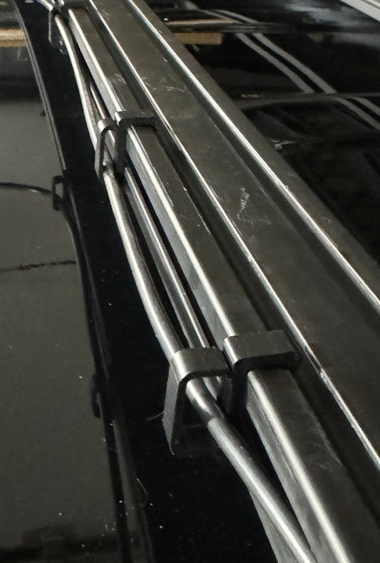 A set of four black ABS plastic cable management clips of varying sizes, designed for use with roof rack cross bars.