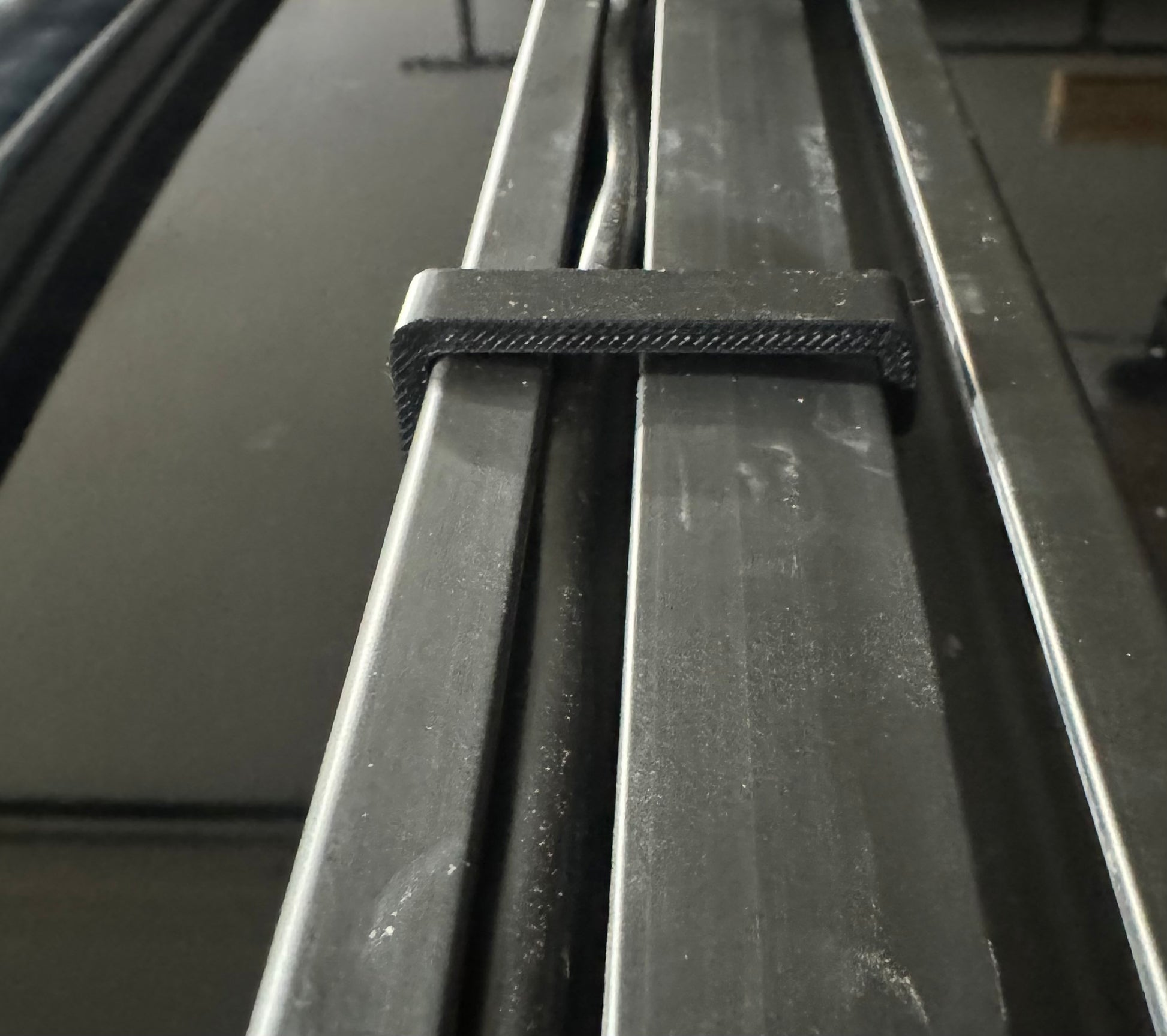 A black plastic cable management keeper installed on a vehicle's roof rack cross bar.