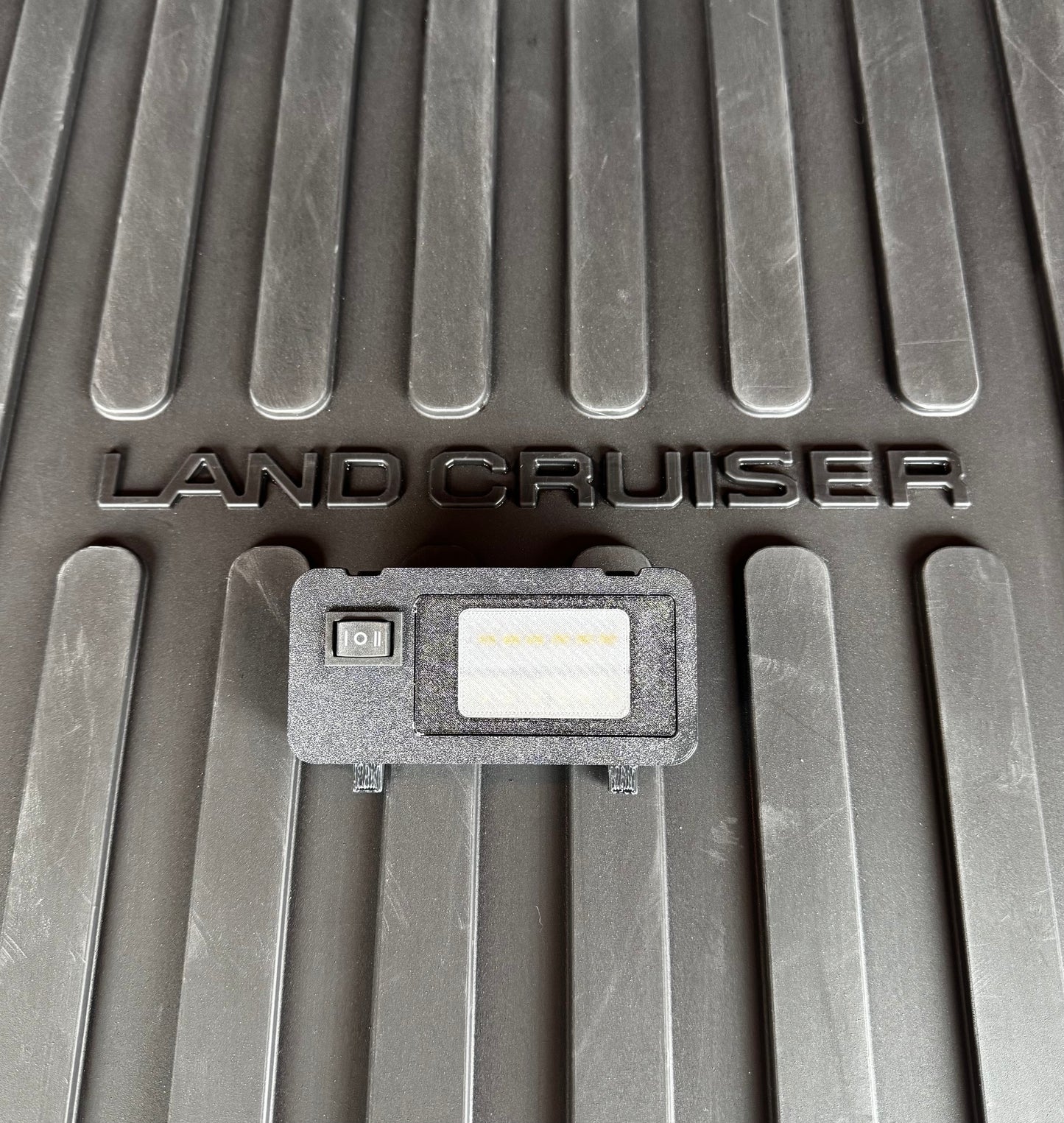 A switchable LED hatch light for Land Cruiser LC250/GX550 placed on a textured surface with the text 'LAND CRUISER' visible.