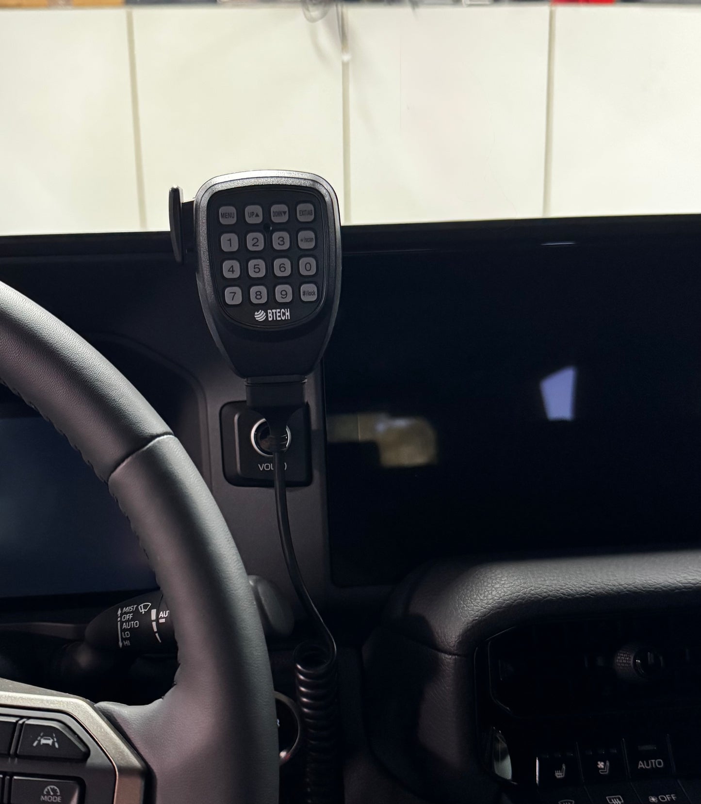 Car dashboard with a microphone and control panel, mounted on a tiled wall background.