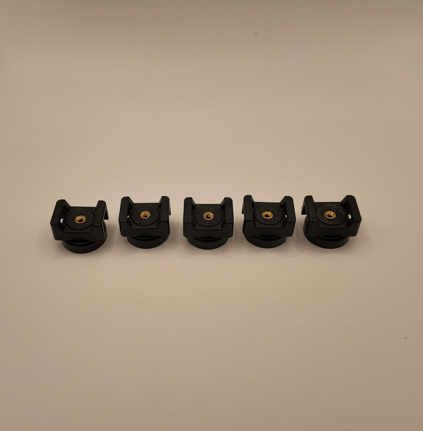 Five black plastic components with gold screws on a beige background