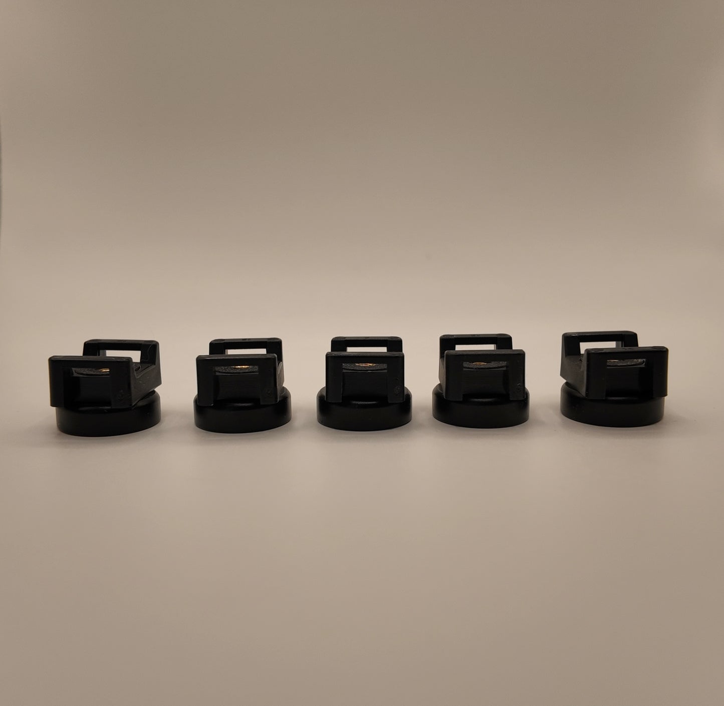 five black cylindrical objects with handles arranged in a row on a beige background
