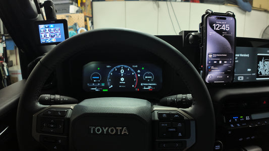 Steering wheel of a Toyota vehicle with multiple smartphones mounted on the dashboard displaying different apps.