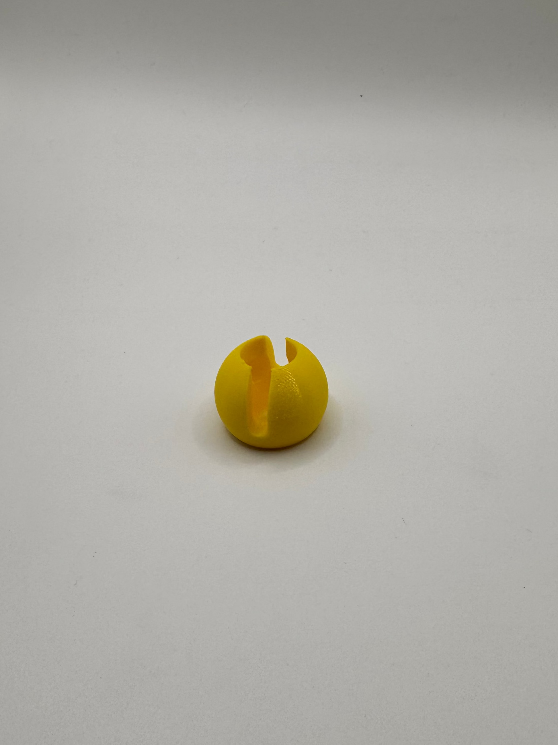 A small yellow plastic ball with a vertical slit through the center, placed on a plain light gray background.