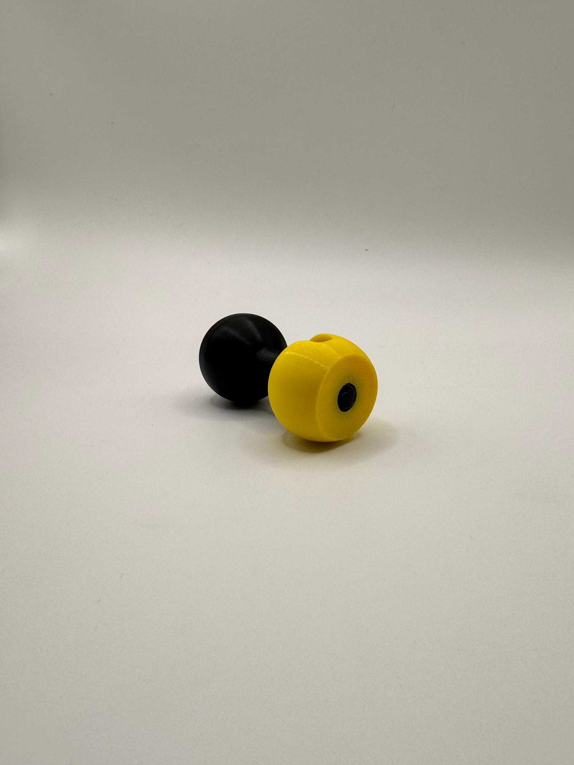 A small novelty item consisting of two round, matte-finish pieces: one black and one bright yellow, placed on a plain light gray studio background.