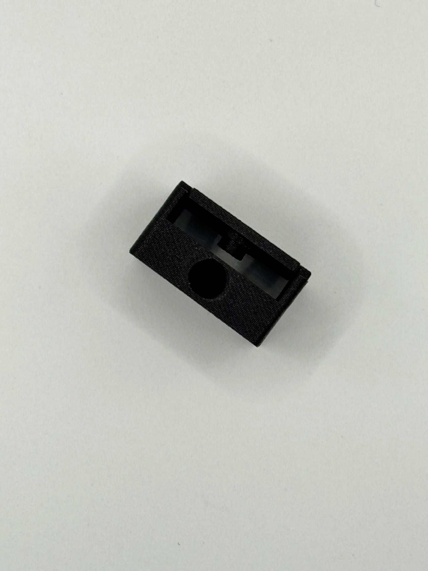 A small black textured plastic component with a circular hole, photographed on a plain light gray background.