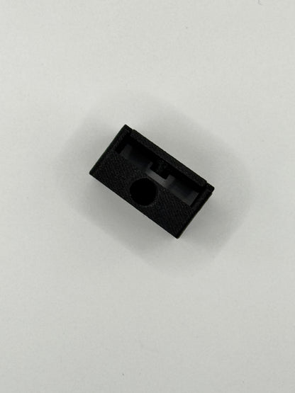 A small black textured plastic component with a circular hole, photographed on a plain light gray background.