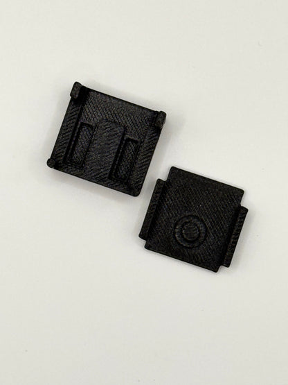 Two small black textured plastic components with rectangular slots and a circular detail, shown on a plain white background.