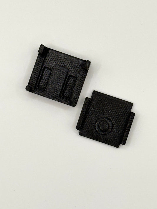Two small black textured plastic components with rectangular slots and a circular detail, shown on a plain white background.