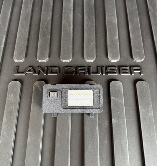 A switchable LED hatch light for Land Cruiser LC250/GX550 placed on a textured surface with the text 'LAND CRUISER' visible.