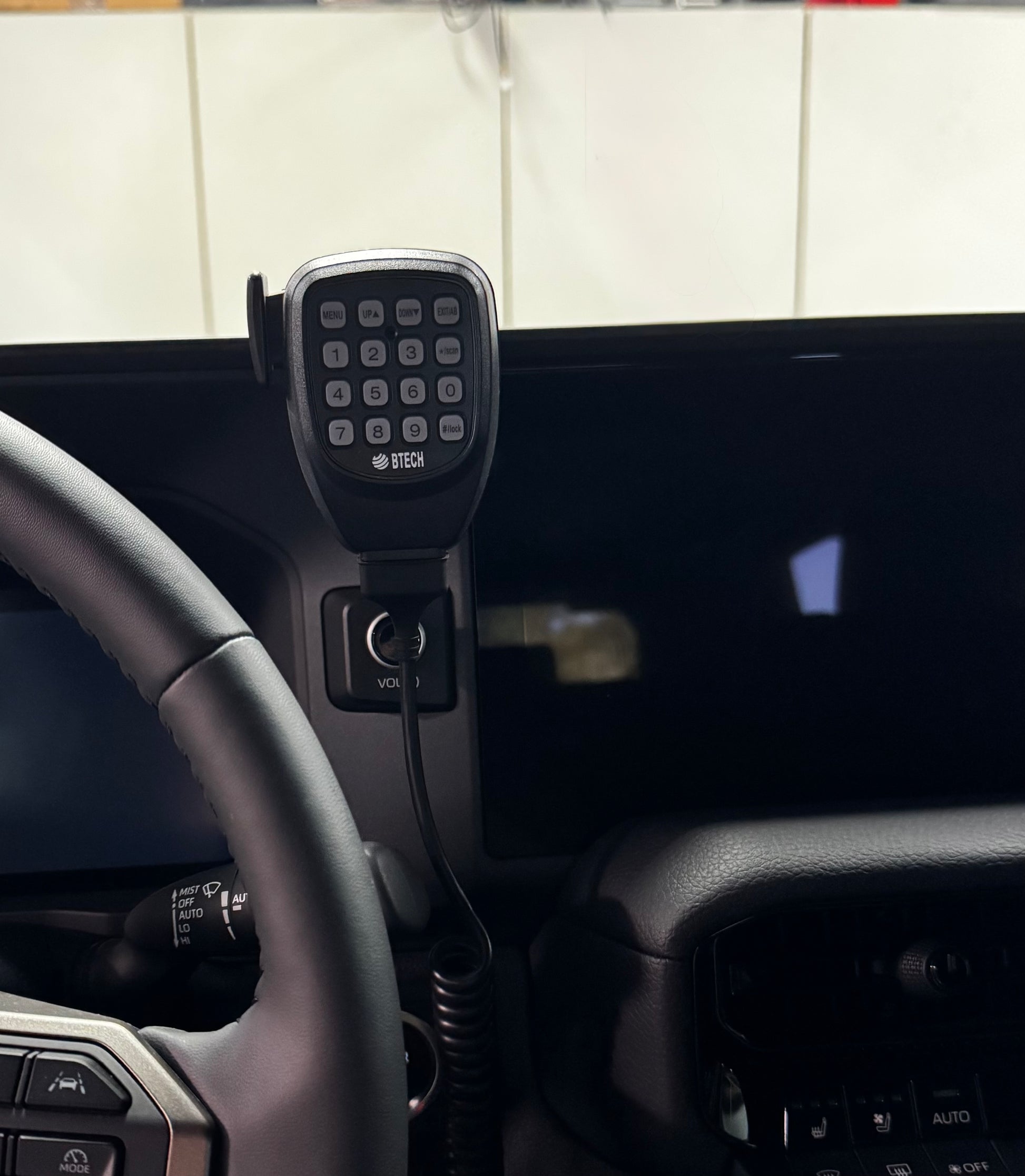 Car dashboard with a microphone and control panel, mounted on a tiled wall background.