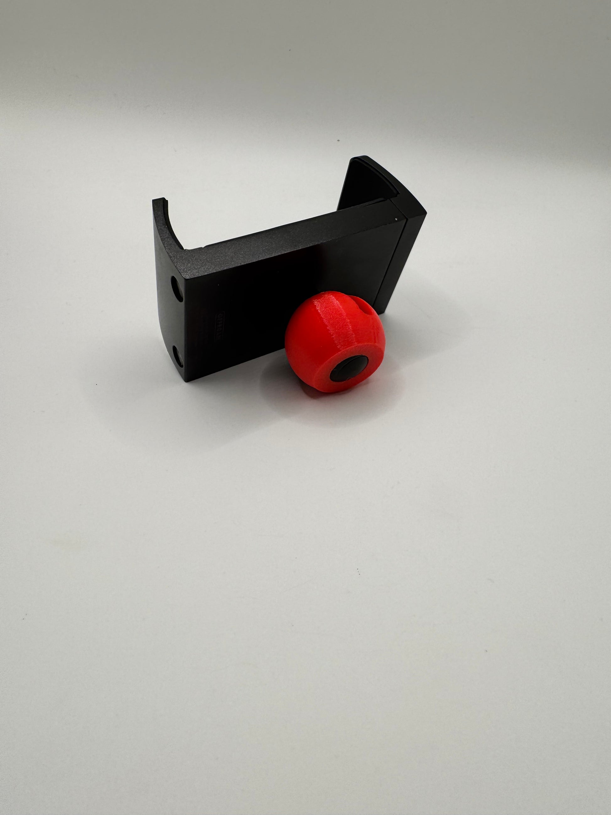 A black plastic mounting bracket with a red spherical knob or cap, photographed against a plain light gray background.