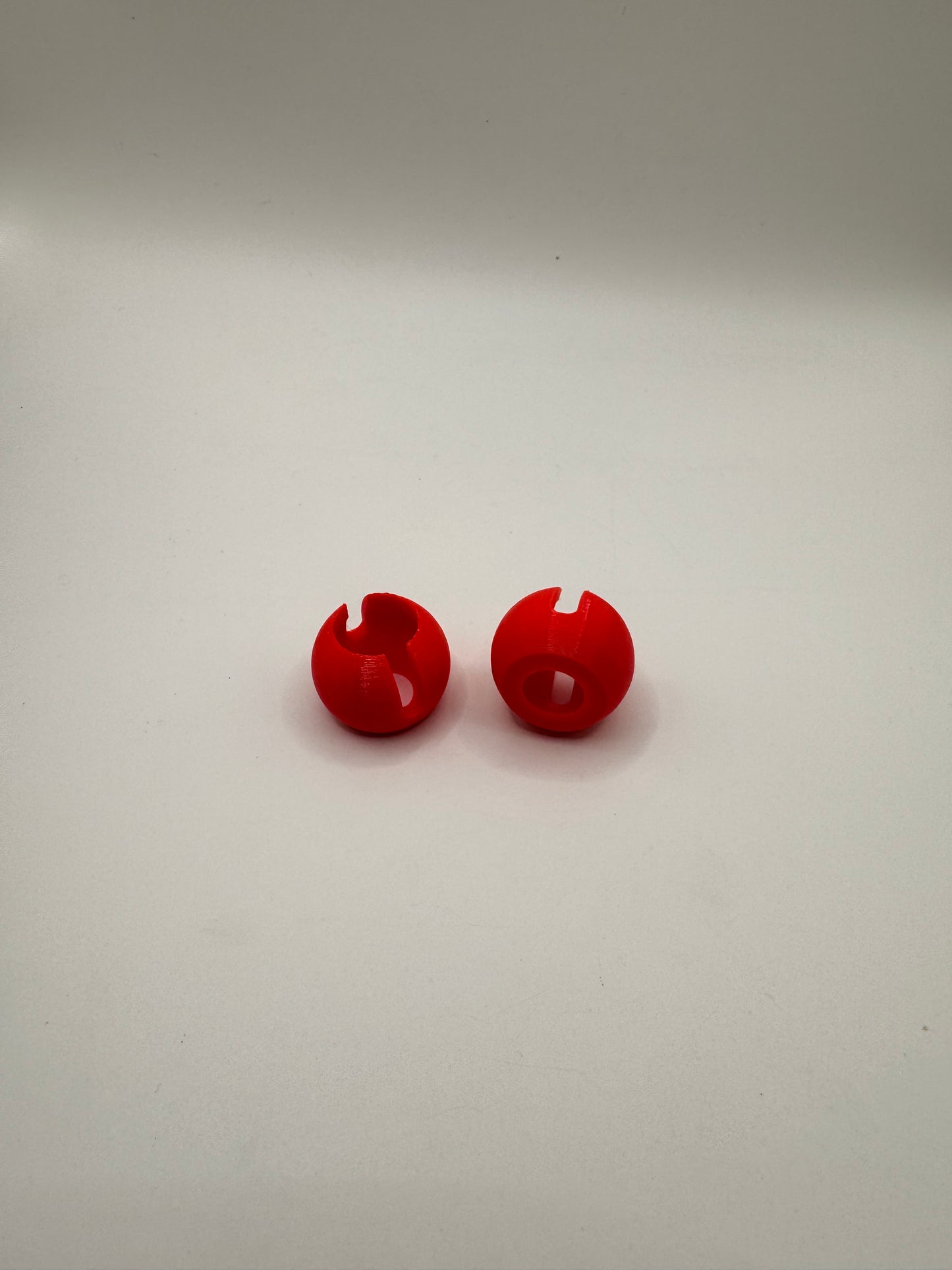 Two small glossy red plastic snap hooks or wall pegs displayed vertically on a plain off-white background.