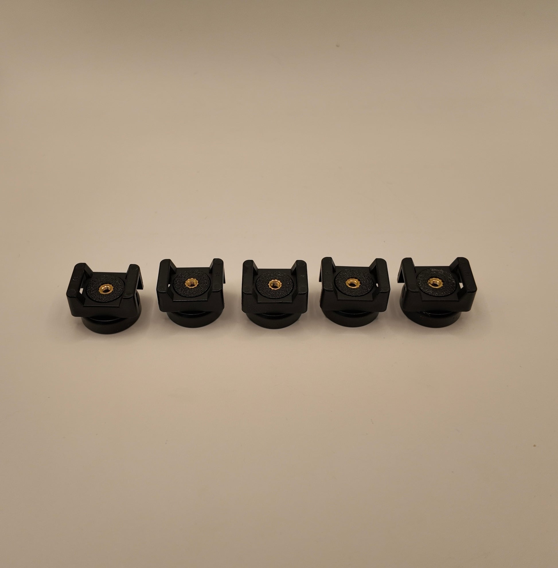Five black plastic components with gold screws on a beige background