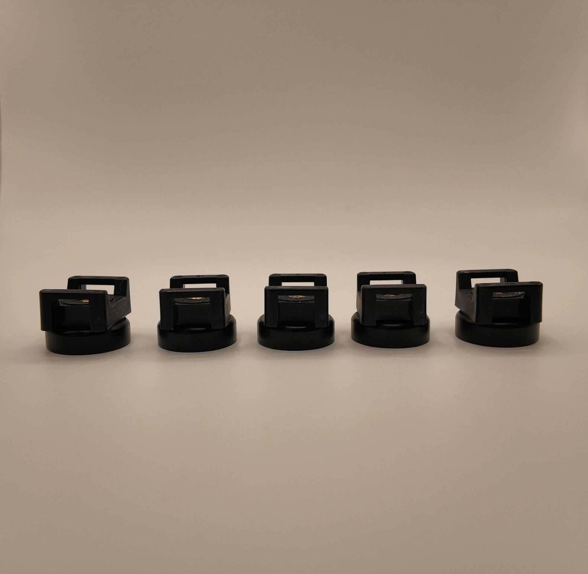five black cylindrical objects with handles arranged in a row on a beige background